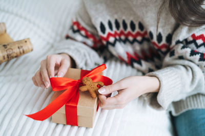 Crop photo of young woman in nordic sweater packing gift box at home