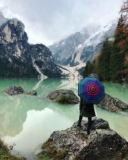 Rear view on woman standing with umbrella on rock in lake against mountains