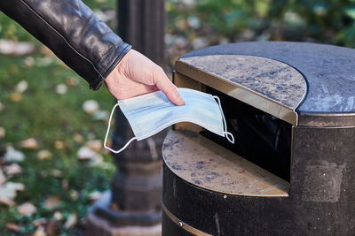 A man is putting a used medical mask into a trash bin.