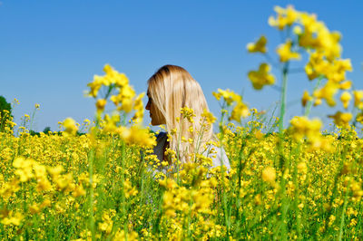 Young woman standing amidst field against clear sky