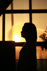Silhouette woman standing against window at sunset
