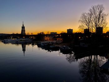Silhouette buildings by river against sky during sunset