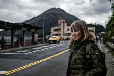 Portrait of woman standing on road at jiufen against the view of keelung mountain in the background.