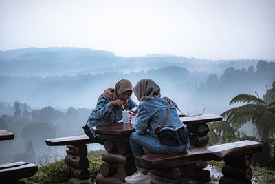 People sitting on mountain against sky during winter