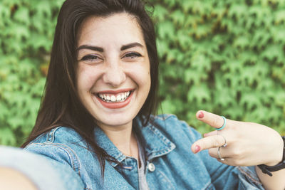 Portrait of smiling young woman gesturing against plants