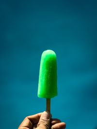 Close-up of hand holding ice cream against blue background