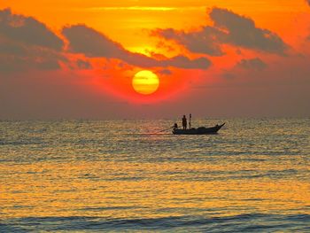 Silhouette people sailing on sea against orange sky