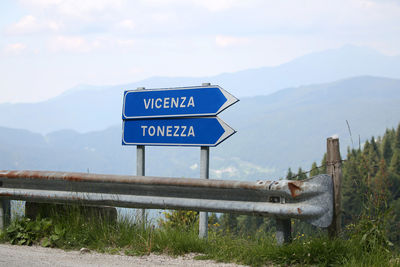 Information sign on road by mountains against sky