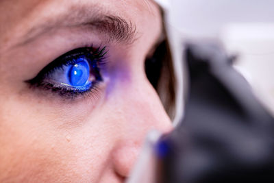 Closeup female patient with eye illuminated with blue light waiting for tonometer to finish measure intraocular pressure during eye examination in clinic