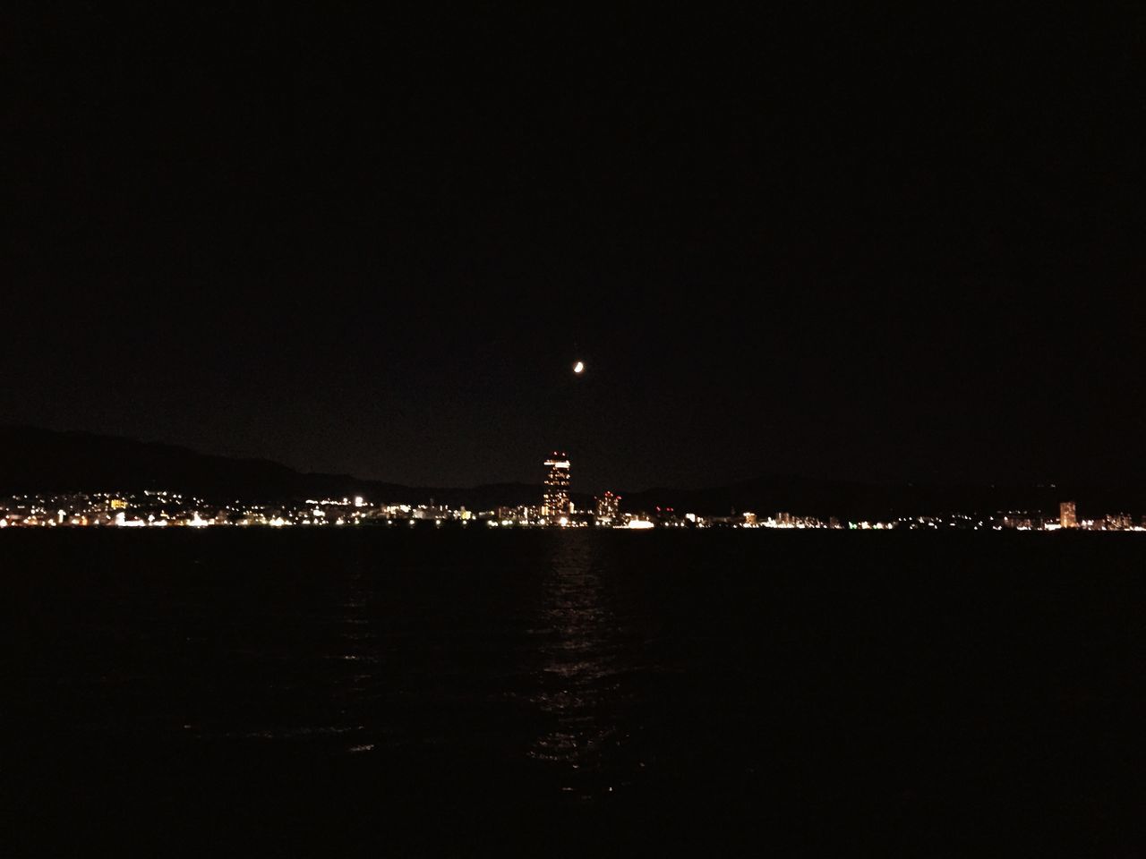 night, illuminated, water, city, copy space, sea, cityscape, built structure, waterfront, architecture, building exterior, dark, river, clear sky, lighting equipment, reflection, light, sky, light - natural phenomenon, glowing