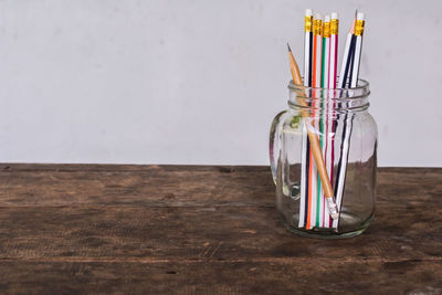 Close-up of pencils in glass jar on table against white wall