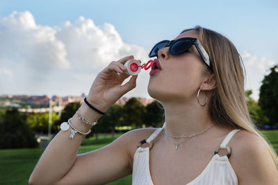 Close-up of woman blowing bubble against sky