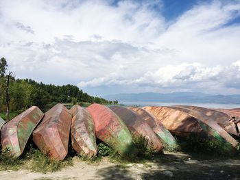 Upside down boats at beach against cloudy sky