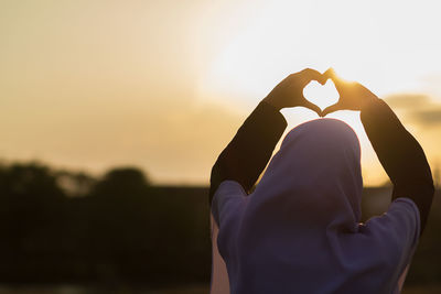 Rear view of silhouette man holding heart shape against sky during sunset