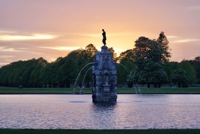 Statue by trees against sky during sunset