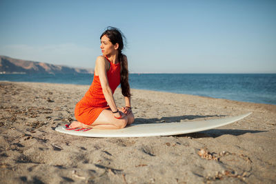 Young woman sitting on shore at beach against sky