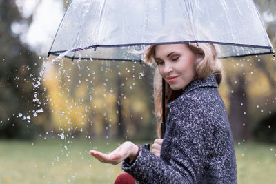 Young woman enjoying rain while holding umbrella at public park