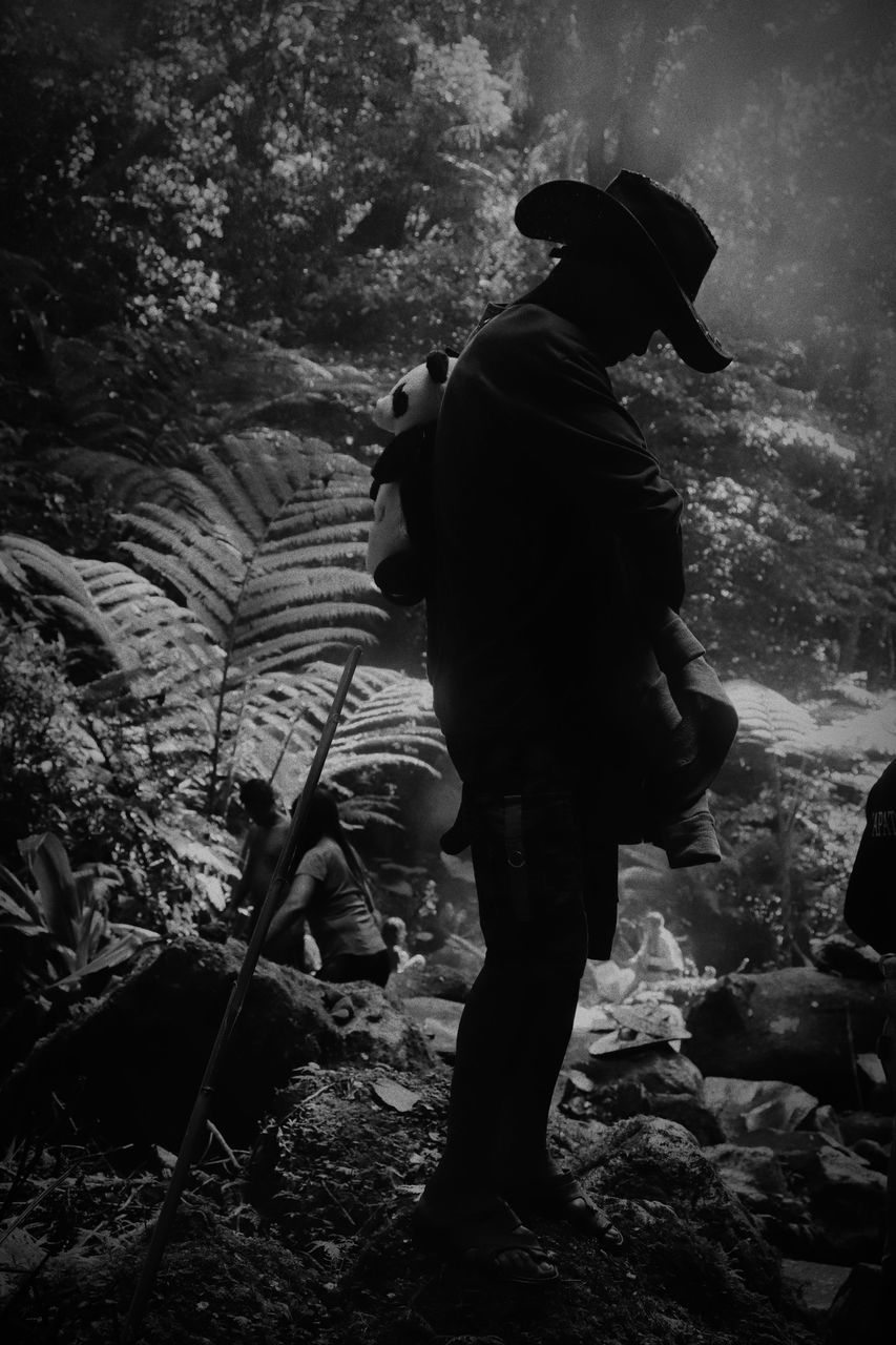 REAR VIEW OF MAN STANDING ON ROCK AT LAND