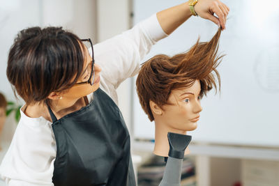 Hairstylist with the hair dryer in hands explaining hairstyling techniques, using mannequin head