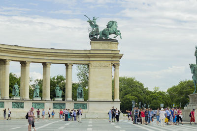 People at heros square against cloudy sky