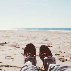 Low section of person with shoes on beach during sunny day