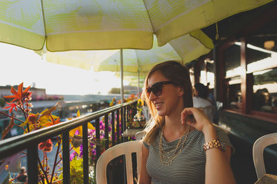 Happy young woman sitting by railing in restaurant