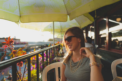 Happy young woman sitting by railing in restaurant