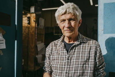 Portrait of senior male carpenter near workshop doorway during sunny day