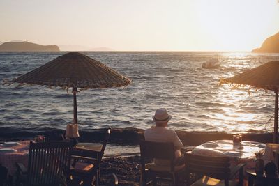 Rear view of people on shore against sky during sunset