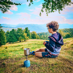 Rear view of boy sitting on land against sky