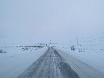 Snow covered road by electricity pylon during winter