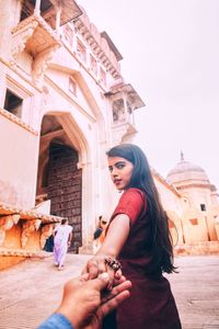 Cropped hand holding woman on walkway by historic building