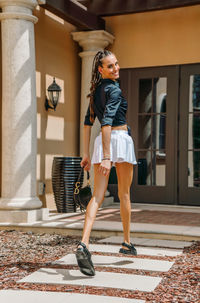 Full length portrait of young woman against building