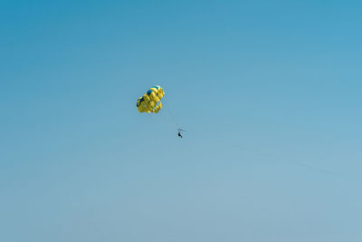 Low angle view of people paragliding against clear blue sky