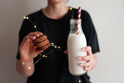 Woman holding tasty cookies and bottle of fresh milk over glowing lights close up. winter holiday