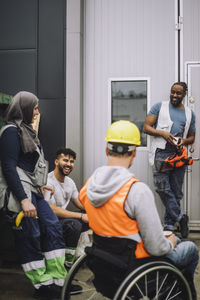 Happy young construction worker talking with male and female colleagues during break at site