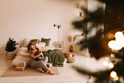 A pretty girl in pajamas rejoices and smiles during the christmas holidays in cozy bedroom interior