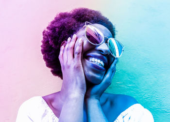 Close-up of smiling woman wearing sunglasses against wall