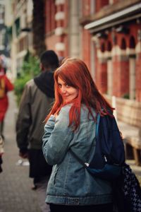 Redhead woman smiling while standing on sidewalk in city