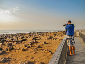 Rear view of man photographing seals on beach, cape cross seal reserve, south africa