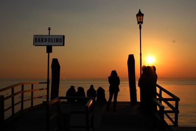 Silhouette people on pier over sea during sunset