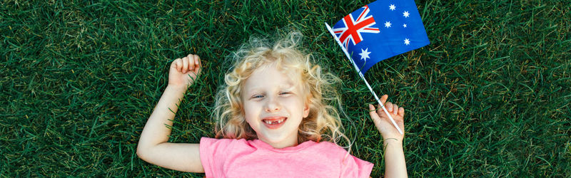 High angle portrait of cute girl holding australian flag lying on grass