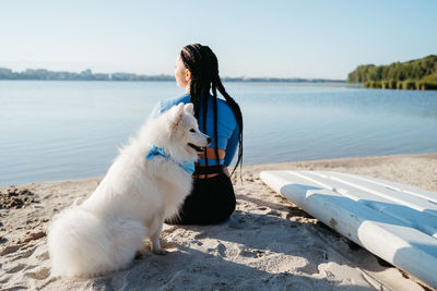 Woman with locs sitting on the beach of city lake with her best friend, dog breed japanese spitz