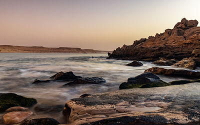 Rocks on beach against sky during sunset