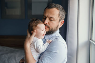 Side view of man playing with daughter while holding by window