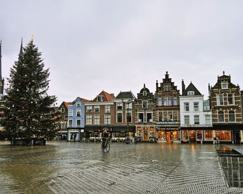 Buildings by wet street against sky in city during christmas