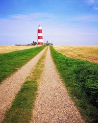 Road leading towards lighthouse amidst field against sky