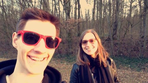 Portrait of smiling young woman wearing sunglasses against trees