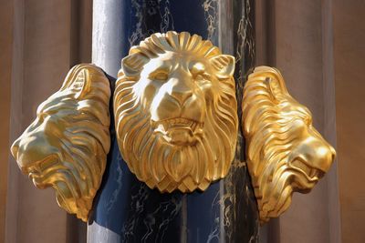 Close-up of gold colored lion face sculpture on column