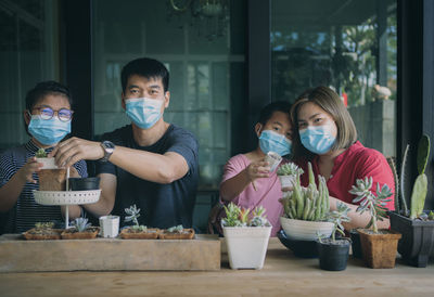 Portrait of cheerful family wearing mask holding succulent plants on table